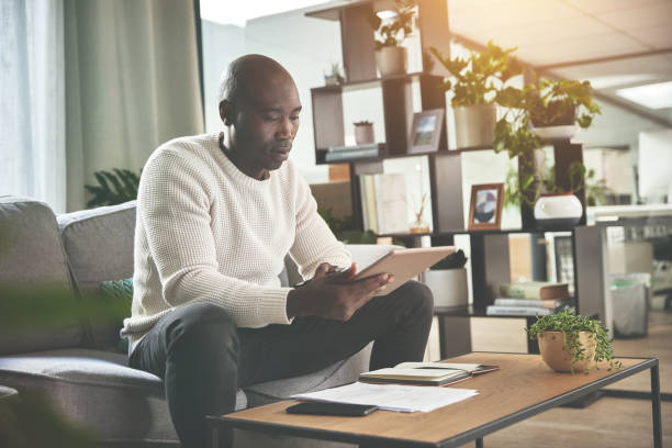 istock A man using a digital tablet and working with paperwork at home. A young man paying bills, planning his finance online with a touchscreen on the sofa 1399934951