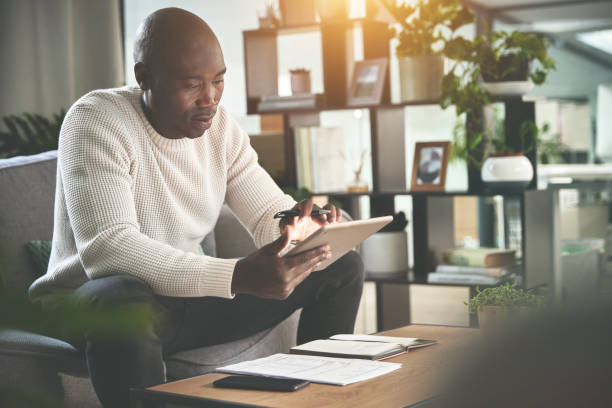 istock A man using a digital tablet and working with paperwork at home. A young man paying bills, planning his finance online with a touchscreen on the sofa 1399935514