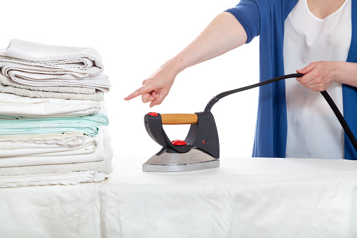 A woman jokingly commands bite to ironing a pile of laundry while holding the iron by the electric wire