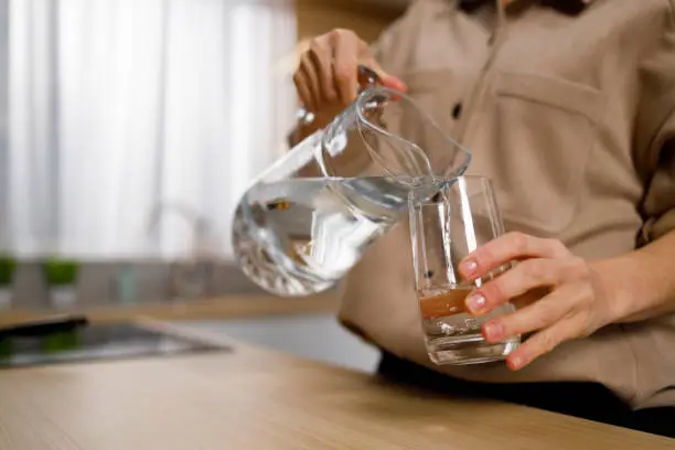 Close up view of woman pouring water from jug into glass in kitchen