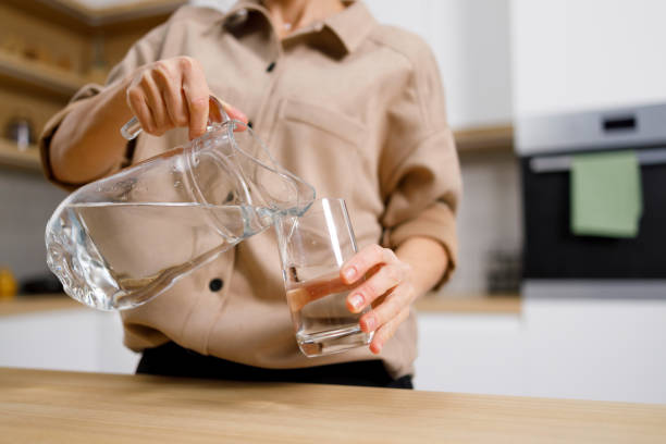 visão de perto de uma mulher que derrama água limpa de um jarro em vidro - pouring water carafe glass - fotografias e filmes do acervo