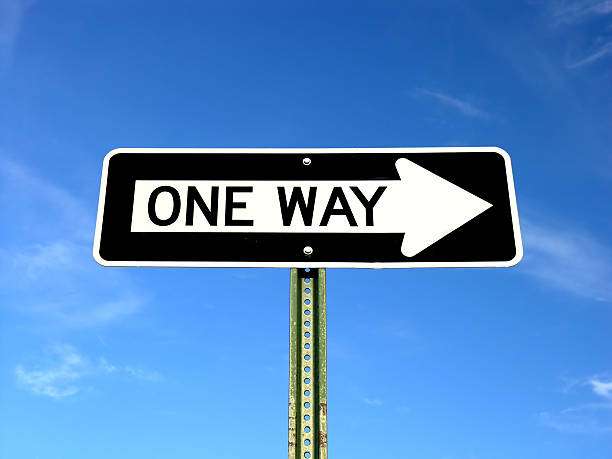 Black and white one way sign with blue sky One way sign isolated against a blue sky one way stock pictures, royalty-free photos & images