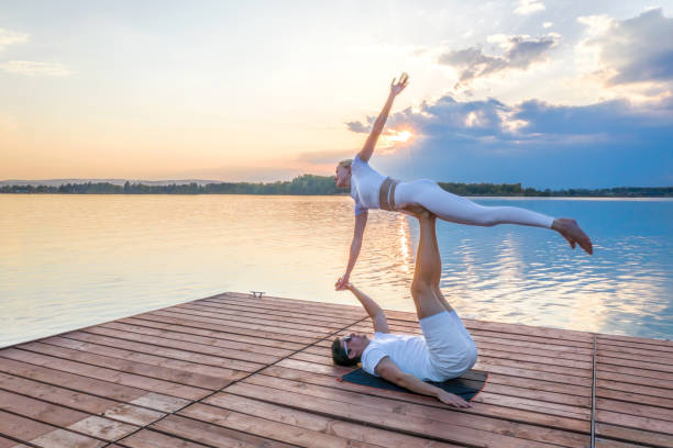Beautiful young couple doing acro yoga on the pier against sunset. Man lying on the pier and balancing woman in his feet. Beautiful young couple doing acro yoga on the pier against sunset. Man lying on the pier and balancing woman in his feet. acroyoga stock pictures, royalty-free photos & images