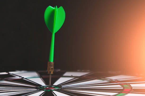 istock Dartboard with green dart stuck in the center with bright blue light. 1399942082
