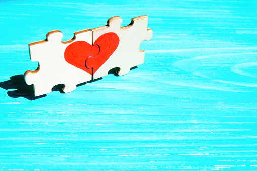 Heart symbol made from two matching jigsaw puzzle pieces on a blue wooden background. Creative romantic concept.