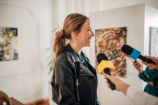 Young female artist talking to the press at gallery opening.