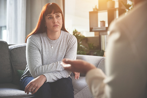 A woman talking to a psychologist or therapist. A young woman looking sad while getting help during a therapy session with a counsellor