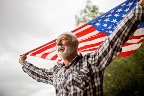 patriote américain mature souriant tenant le drapeau des états-unis - fourth of july honor freedom square photos et images de collection