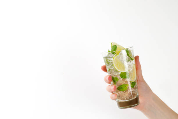 Glass with cold cocktail mojito in a woman hand. Lemonade with ice, lime and mint. Fresh  tonic in hand on white background. Glass with cold cocktail mojito in a woman hand. Lemonade with ice, lime and mint. Fresh  tonic in hand on white background. highball glass stock pictures, royalty-free photos & images