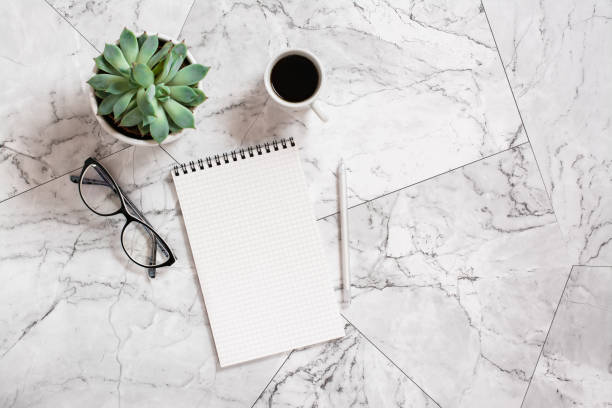 istock Notebook, pen, glasses, succulent and a cup of black coffee on a marble tile. 1399951638
