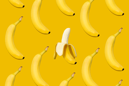 Bananas flat lay on yellow background with one peeled banana in center