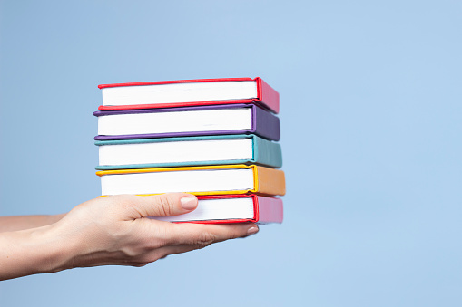 Woman hands holding pile of books over light blue background. Education, self-learning, book swap, hobby, relax time