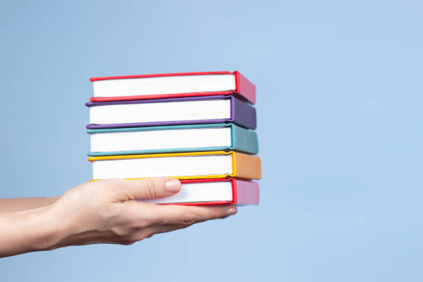 Female hands holding pile of books over light blue background. Education, self-learning, book swap, hobby, relax time stock photo