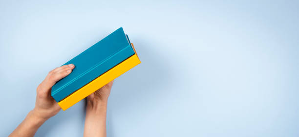 Female hands holding two blue and yellow color books over light blue background. Education, self-learning, book swap Female hands holding two blue and yellow color books over light blue background. Education, self-learning, book swap. ukrainian language stock pictures, royalty-free photos & images
