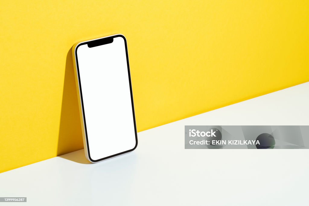 Blank screen smart phone mockup, template Blank white screen smart phone mockup, template with clipping path on yellow and white background. Phone leaning against to yellow wall. Brand Name Smart Phone Stock Photo