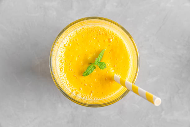 istock Fresh yellow summer mango smoothie in a glass with a straw and mint on gray concrete table. Top view 1399956957