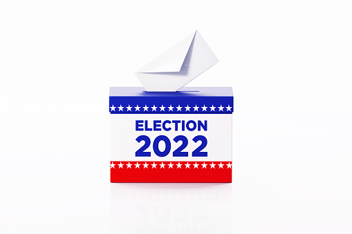 Election 2022 written ballot box textured with American flag. Isolated on white background. A vote envelope is entering into the ballot box. Horizontal composition with copy space. Great use for referendum and presidential elections related concepts. Clipping path is included.