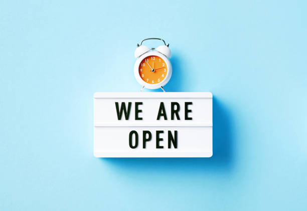 istock Alarm Clock And We Are Open Written White Lightbox Sitting On Blue Background 1399958226