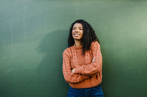 Portrait of a happy young African-American woman with arms crossed against green wall