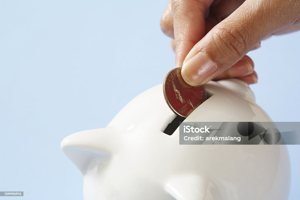 Woman dropping quarter into white piggy bank A woman saving a coin into a piggy bank Adult Stock Photo