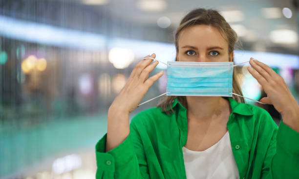 Woman putting on a medical mask in the mall. Wear a mask in public place. stock photo