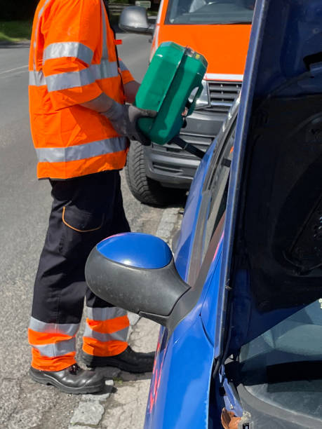 close-up image of blue car broken down on roadside, refilling fuel tank with jerry can of fuel, vehicle breakdown assistance, car mechanic wearing reflective, high visibility jacket - gas can stranded gasoline car imagens e fotografias de stock