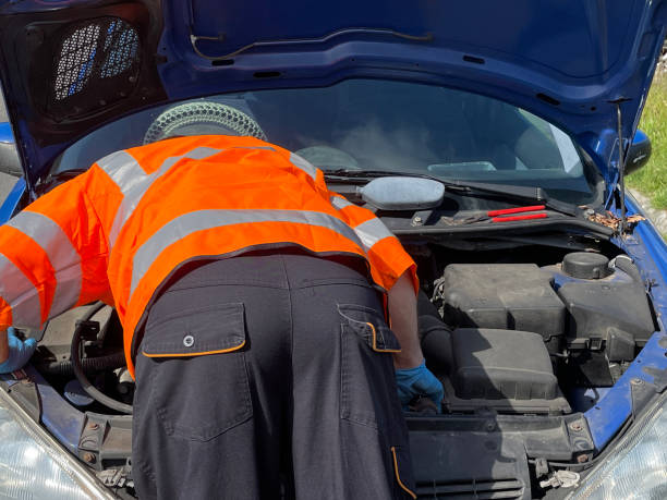 istock Close-up image of blue car broken down on roadside, open car bonnet displaying engine being repaired by vehicle breakdown assistance, car mechanic wearing reflective, high visibility jacket 1399959812