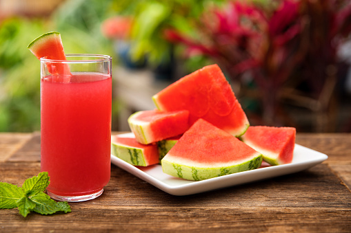 This is an outdoor photograph of a plate of sliced triangle watermelon sitting on a plate of a plate of sliced triangle watermelon sitting on a plate with a glass of watermelon juice and mint