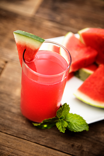 This is an outdoor photograph of a plate of sliced triangle watermelon with a glass of watermelon juice and mint