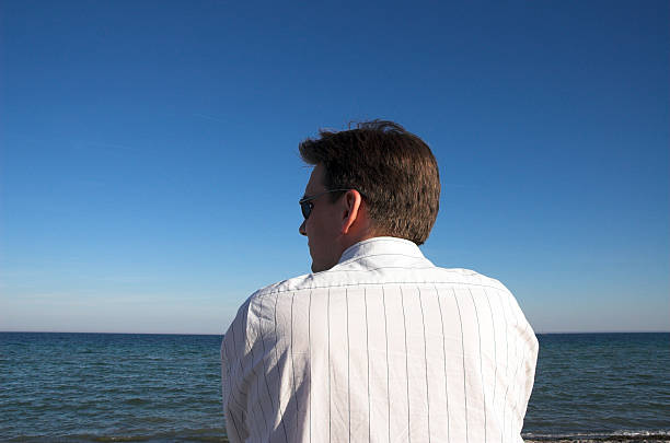 Businessman recharging Man in white striped shirt and sunglasses in front of the sea, looking left. alintal stock pictures, royalty-free photos & images