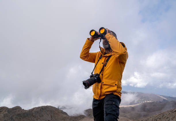 Outdoor photographer looks through binoculars enjoying spectacular view on top of the mountain stock photo