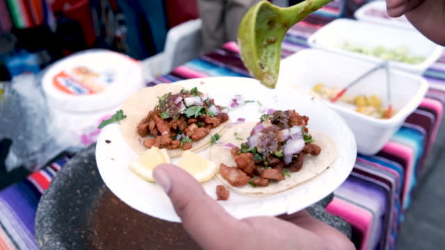 Client puoring salsa over a al pastor taco at a taco stand