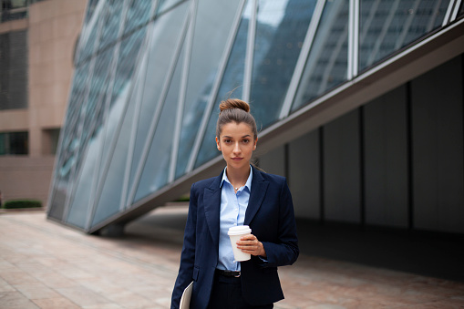 Businesswoman Walking Along Street Holding Takeaway Coffee and Digital Tablet in Hong Kong