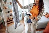 Woman is steaming blue stripped shirt in room