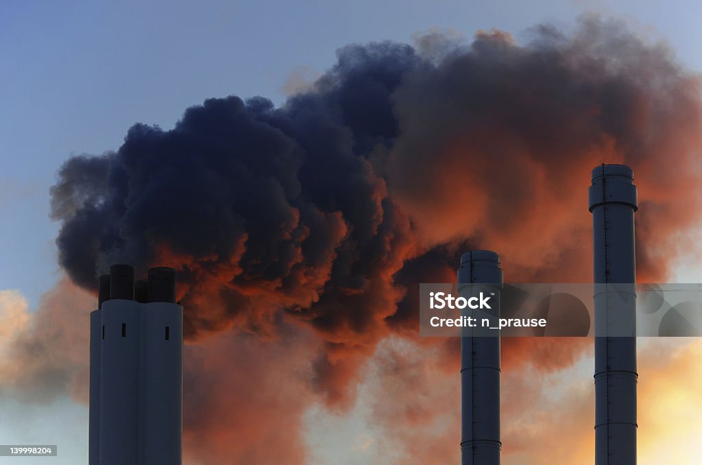 Chimneys Pollution concept of smoking chimneys. The setting sun illuminates the vapor from below, giving it an ominous impression, like that of volcano smoke. Air Pollution Stock Photo