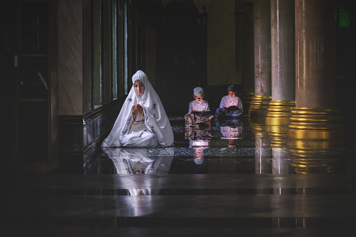 muslim people woman in hijab and muslim boys praying and reading holy quran or kuran book together in mosque
