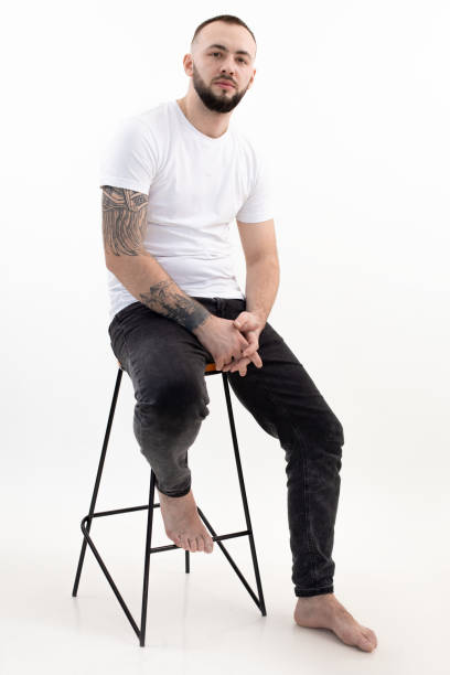 istock Vertical of tattooed handsome dark-haired, confident, bearded barefoot man sit on chair. Fashionable modern hipster 1399986977