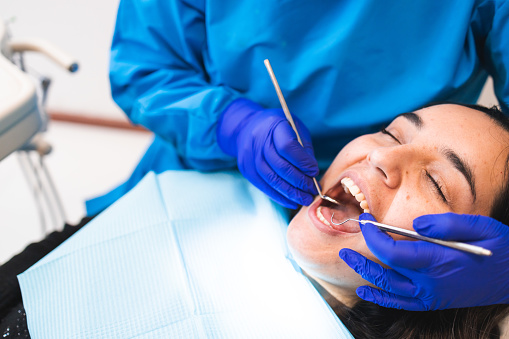 Unrecognizable dentist doing a routine dental checkup using a mouth mirror and an excavator, to a female patient. Dental care. Horizontal. Copy space