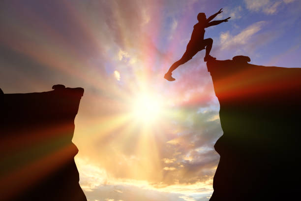 istock silhouette man jumping over a precipice between two rocky mountains at sunset. Freedom, risk, challenge, success concept. 1399995691