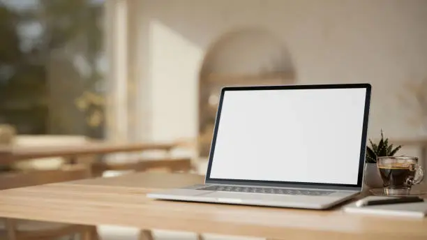 Photo of Laptop computer on wooden tabletop over blurred modern minimal cafe in background.
