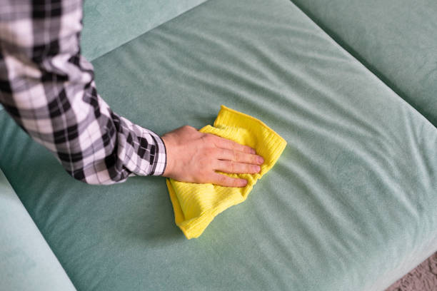 worker with yellow microfiber rag cleaning sofa textile at home stock photo