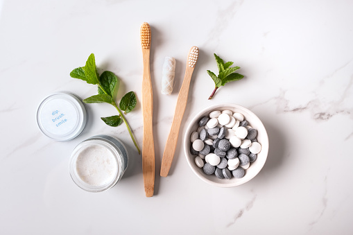 Zero waste, recyclable and compostable dental health products:  Bamboo toothbrushes and dental floss, vegan peppermint and charcoal toothpaste tablets, zero waste toothpaste in jar and sprigs of fresh mint.