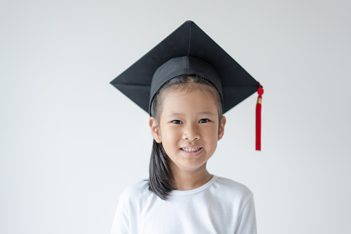 Smiling happy Asian school girl wearing graduation cap. Concept of education using Asia kid and white background.