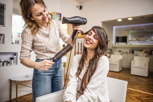 Photo of a hairdresser blow drying hair of her customer in a hair salon.