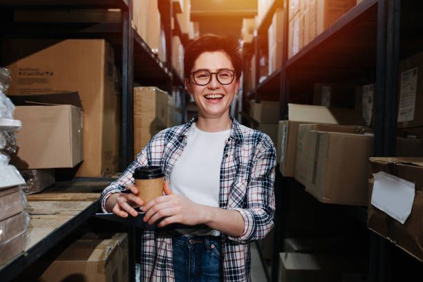 portrait d’une joyeuse employée d’entrepôt debout entre les étagères - giving file document stack photos et images de collection