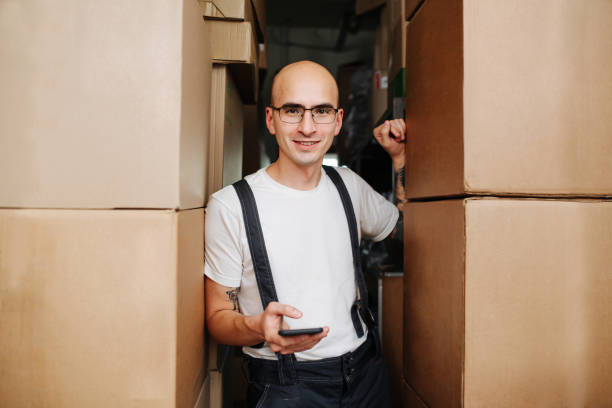 un employé d’entrepôt confiant entre des piles de boîtes, regardant la caméra - giving file document stack photos et images de collection