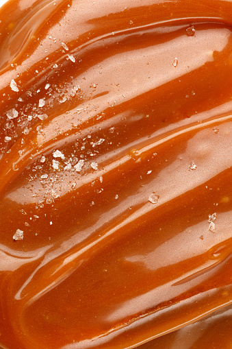 Liquid salted caramel syrup. Background of salted caramel paste. Texture Close up, top view. Sea salt pieces on caramel.