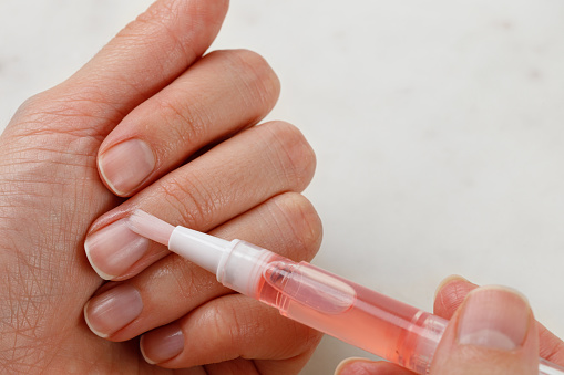 Aplicación de aceite de cutícula. Cuidado de uñas y manicura. Uñas naturales de mujer. Fondo blanco. photo