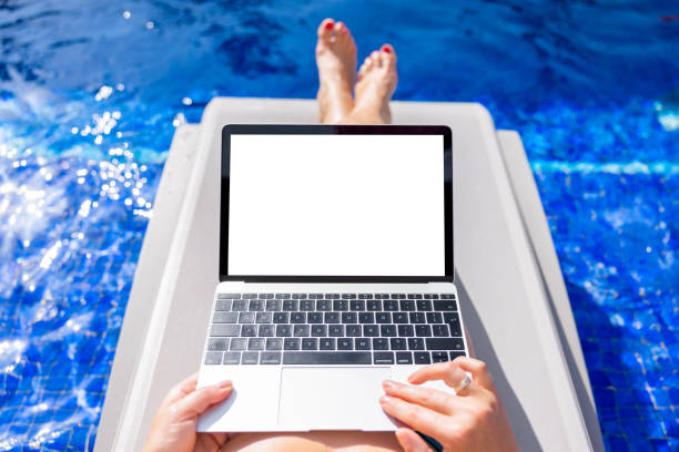 istock Woman using laptop computer on vacation while relaxing by the pool, empty white screen mockup 1400016395