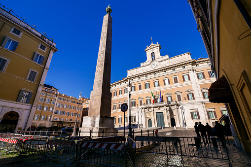 A wide view of the main facade of the Palazzo di Montecitorio (Montecitorio Palace), seat of the Chamber of Deputies of the Italian Parliament, in the historic heart of Rome. In the center, the obelisk of Psammetich II, coming from the Egyptian city of Heliopolis, brought to Rome in 10 BC on the orders of Emperor Augustus. The palace was built in the Baroque style in the second half of the 17th century, based on a project by Gian Lorenzo Bernini and Carlo Fontana, as the residence of the Ludovisi family. After the unification of Italy in 1861 and the definition of Rome as the capital in 1870, the palace was expropriated and designated as the Parliament of the new national state. At the end of the 19th century Palazzo Montecitorio was enlarged on a project by Ernesto Basile, with the construction of the legislative hemicycle and the northern palace in Liberty style. The Palazzo Montecitorio, in addition to hosting the legislative activity of the deputies, is the institutional seat where the election of the President of the Italian Republic takes place every seven years. In 1980 the historic center of Rome was declared a World Heritage Site by Unesco. Super wide angle image in high definition format.